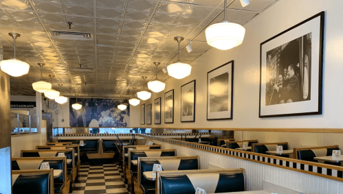 A retro diner interior with checkered floors, green booths, and black-and-white photos on the walls.