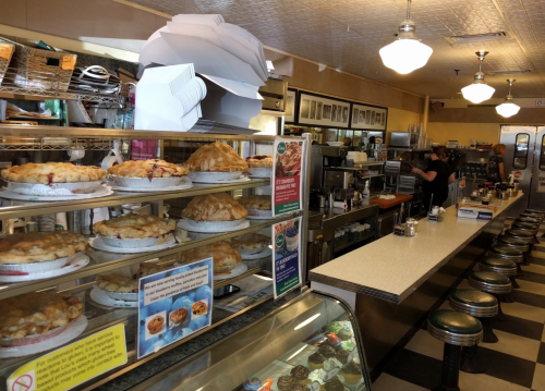 A diner interior featuring a counter, stools, and a display of various pies in glass cases.