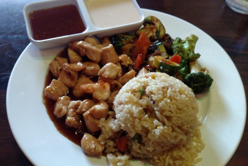 A plate of chicken stir-fry with vegetables, fried rice, and two dipping sauces on the side.