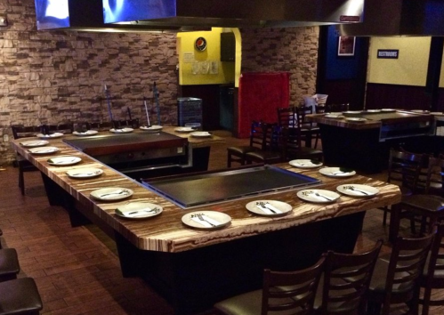 A spacious restaurant interior featuring a large teppanyaki grill table surrounded by empty chairs and plates.