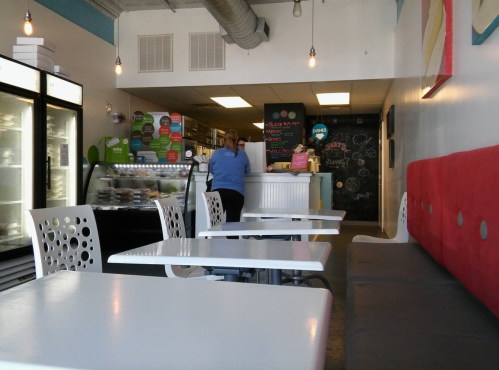 A cozy café interior with white tables, red seating, and a counter where a staff member is serving customers.