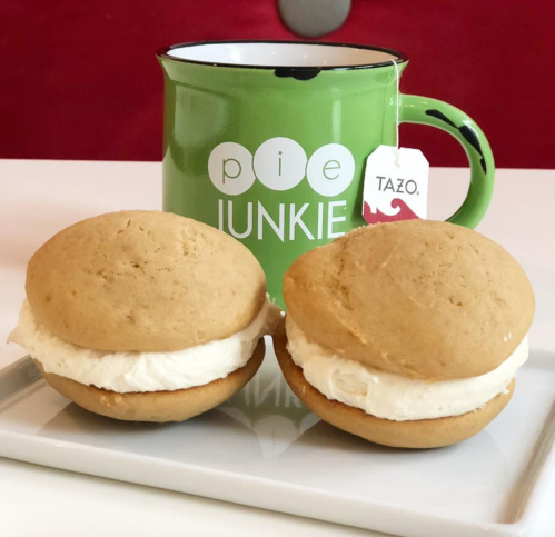 Two cream-filled cookies on a plate next to a green mug labeled "pie junkie" with a Tazo tea tag.