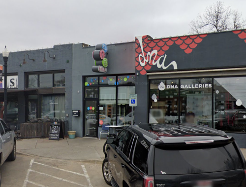 A colorful storefront with a sign reading "dna" and a nearby gallery, featuring a black car parked in front.