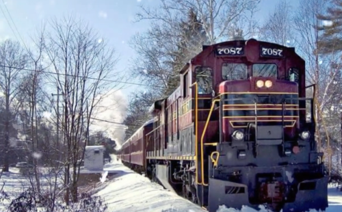 A vintage train travels through a snowy landscape, surrounded by trees and a clear blue sky.