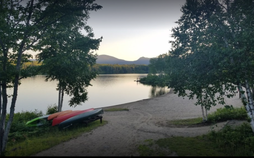 A serene lakeside scene at sunset, featuring kayaks on the shore and mountains in the background.