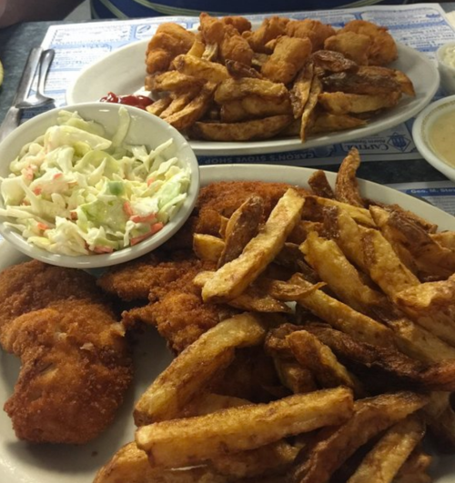 A plate of fried fish, crispy fries, and coleslaw served in a casual dining setting.