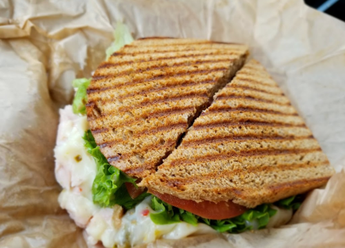 A toasted sandwich with lettuce and tomato, cut in half, resting on crumpled brown paper.