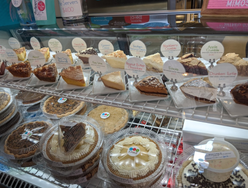 A display case filled with various cakes and pies, including cheesecakes, fruit pies, and chocolate desserts.