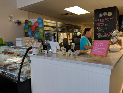 A bakery counter with a display of desserts, a menu board, and a staff member preparing orders.