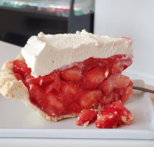 A slice of strawberry pie with a flaky crust, topped with whipped cream and fresh strawberries.