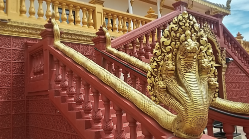 Golden serpent sculptures adorn the red staircase of a temple, featuring intricate designs and ornate railings.