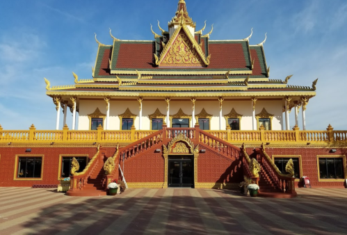 A grand temple with ornate architecture, golden accents, and staircases, set against a clear blue sky.