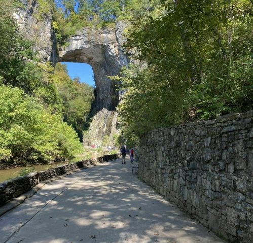 A scenic pathway leads to a large stone arch surrounded by lush greenery and a calm waterway.