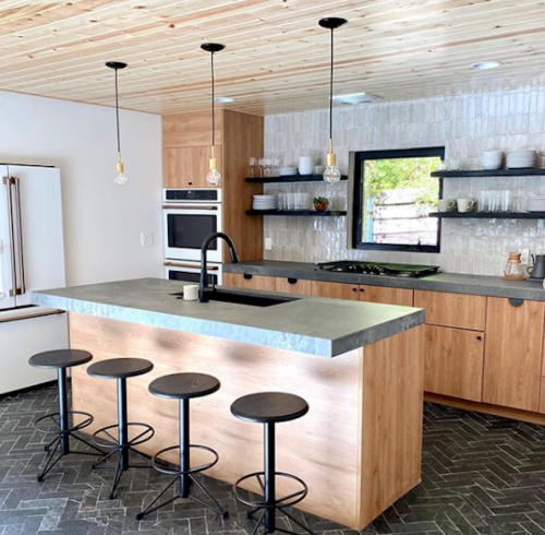 Modern kitchen with wooden cabinets, a concrete island, black stools, and pendant lighting. Sleek and stylish design.