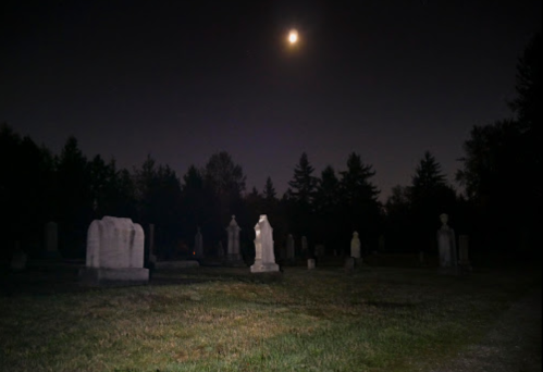 A dark cemetery at night, illuminated by a full moon, with gravestones and trees in the background.