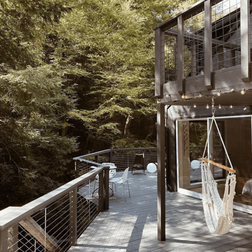 A wooden deck surrounded by trees, featuring a hanging chair and modern outdoor furniture.