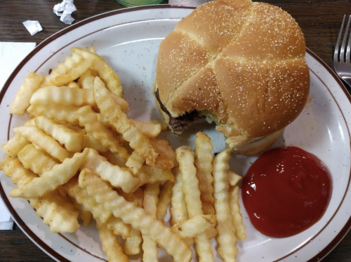 A plate with a half-eaten burger and a side of crinkle-cut fries, accompanied by a small serving of ketchup.