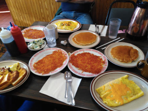 A table set with various breakfast dishes: omelets, pancakes, hash browns, toast, and condiments.