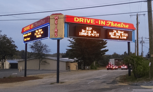Sign for Weirs Drive-In Theatre, displaying "RIP Drive In 1949-9/17" and movie line information. Evening setting.