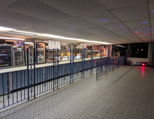 An empty food counter with a blue wall, metal barriers, and colorful lights reflecting on the ceiling.