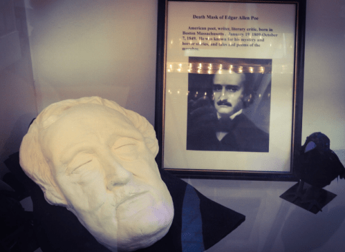 A death mask of Edgar Allan Poe displayed with a framed biography and a portrait of the author.