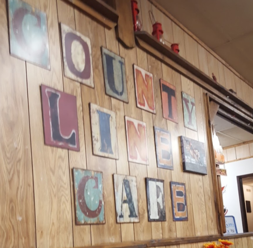 A wooden wall featuring colorful, vintage letters spelling "County Line Cafe." Decor includes small red lanterns.