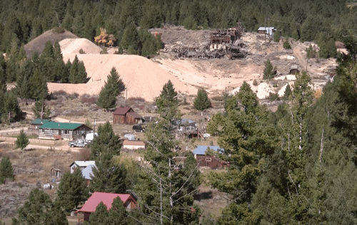 A scenic view of a forested area with small buildings, a mining site, and piles of earth in the background.