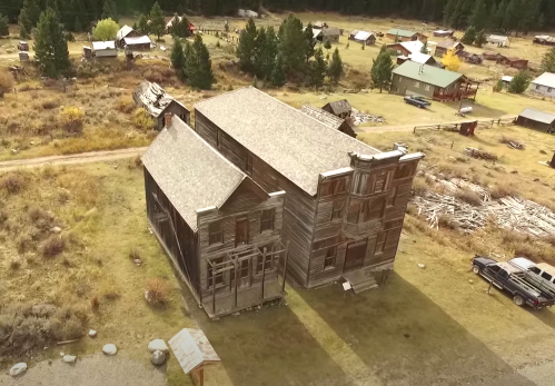 Aerial view of a rustic wooden building in a ghost town, surrounded by trees and scattered structures.