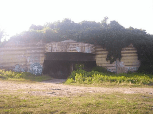 Abandoned building overgrown with vines and vegetation, featuring a large entrance and weathered exterior.