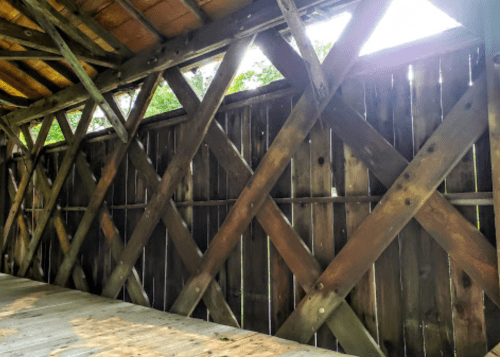 Wooden structure with a diagonal cross-braced wall, sunlight filtering through the gaps, and a wooden floor.