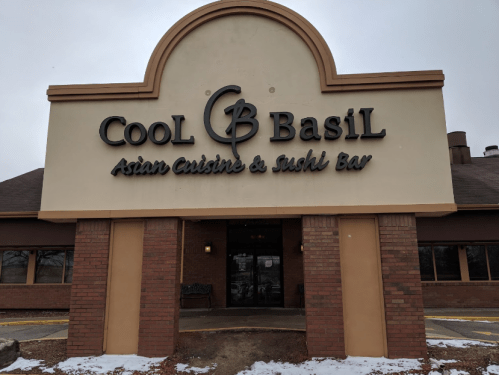 Sign for "Cool Basil Asian Cuisine & Sushi Bar" on a building exterior, with a snowy ground in front.