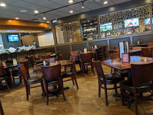 Interior of a restaurant with wooden tables and chairs, featuring a sushi bar and multiple TVs on the wall.