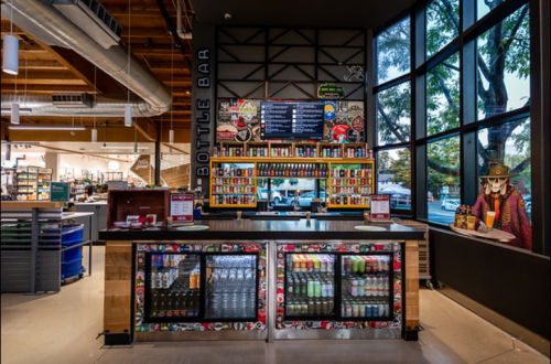 A vibrant bottle bar with a variety of drinks displayed behind a counter, surrounded by large windows and modern decor.