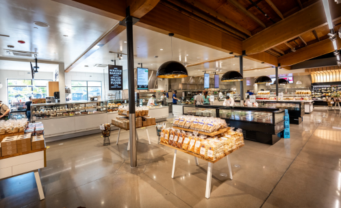 A modern grocery store interior featuring bakery displays, fresh produce, and a spacious layout with wooden accents.