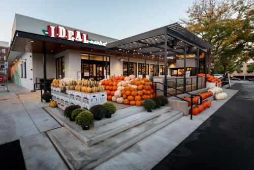 Exterior of a market with a display of colorful pumpkins and gourds at the entrance, surrounded by greenery.