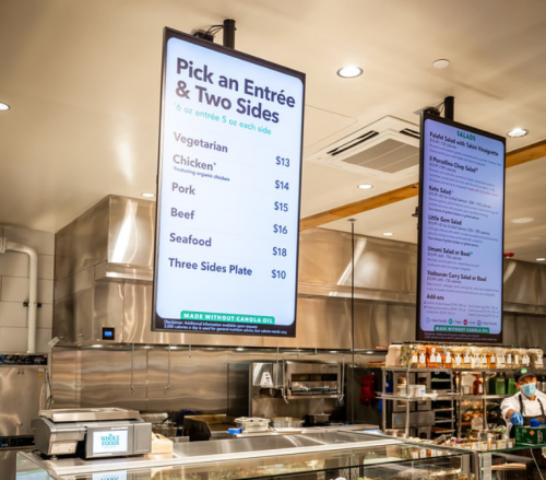 Menu board displaying entrée and side options in a restaurant, with prices for vegetarian, chicken, pork, beef, and seafood.