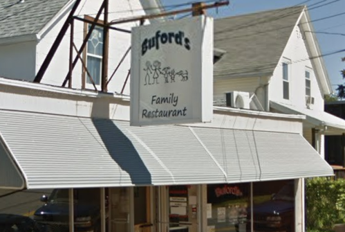 Sign for Buford's Family Restaurant, featuring a simple graphic of people and a dog, with a white building in the background.