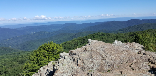 A panoramic view of rolling mountains and lush greenery under a clear blue sky.