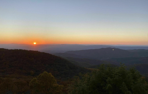 A serene sunset over rolling mountains, with vibrant orange and purple hues illuminating the sky.