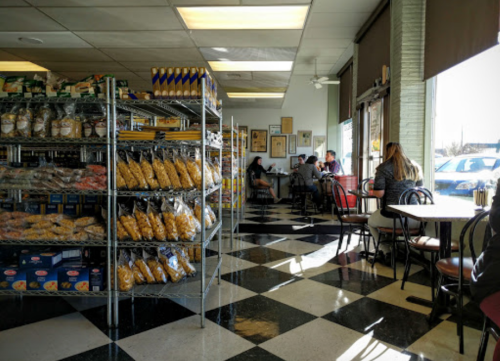 A cozy bakery interior with shelves of baked goods, checkered floor, and customers seated at tables.