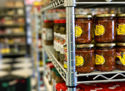 Shelves filled with jars of sauces and pickles in a grocery store, with a blurred background of more products.