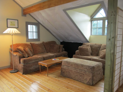 Cozy attic living room with two sofas, a coffee table, and a lamp, featuring wooden floors and sloped ceilings.