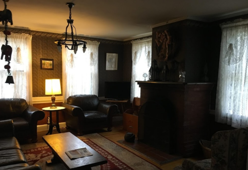 Cozy living room with leather chairs, a wooden table, a fireplace, and large windows with lace curtains.
