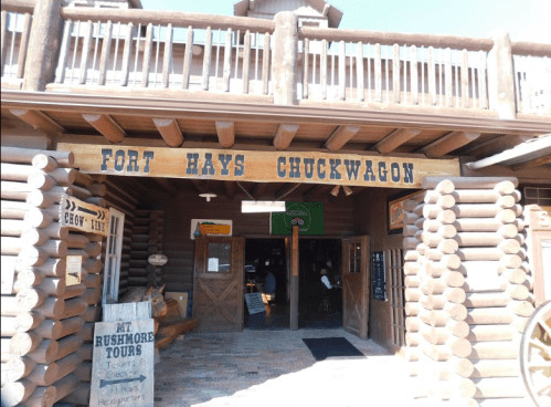 Entrance to Fort Hays Chuckwagon, featuring wooden signage and a rustic log cabin design.