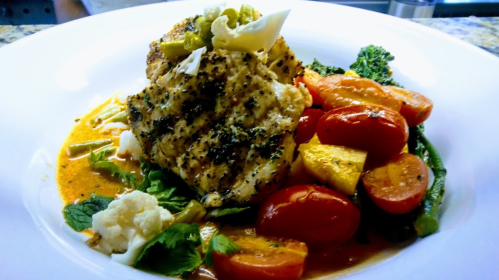 Grilled fish fillet topped with herbs, served with colorful roasted vegetables and a creamy sauce.