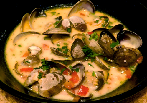 A bowl of clam chowder with clams, diced tomatoes, and herbs in a creamy broth.