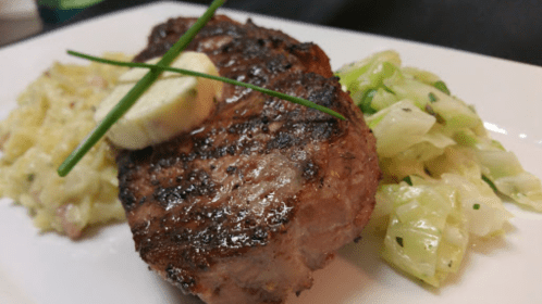 Grilled steak with a pat of butter, served with creamy rice and sautéed cabbage on a white plate.