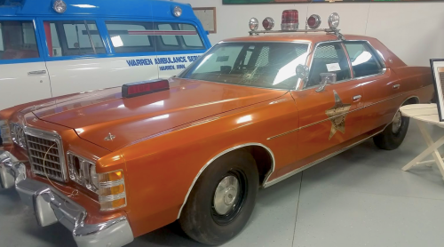 An orange vintage police car with a star emblem and roof lights, displayed in a museum.