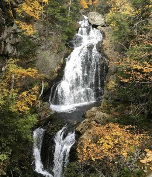 A cascading waterfall surrounded by vibrant autumn foliage and rocky cliffs.