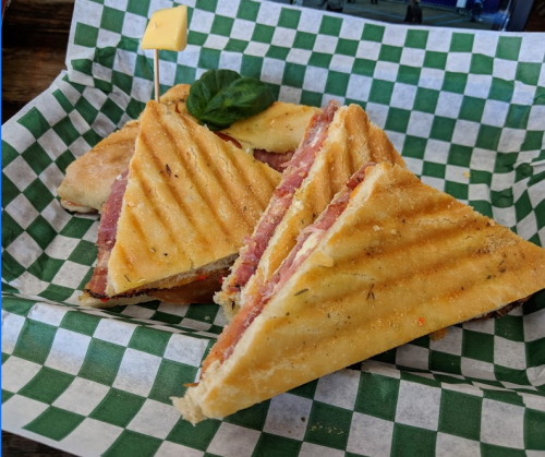 A toasted sandwich cut into triangles, filled with ham and cheese, served in a green and white checkered paper basket.